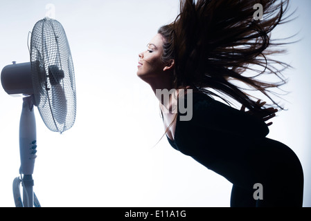 A young woman  wearing black clothes flicking her long hair back over her shoulders in front of a fan in a photo studio