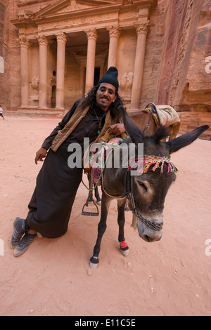 Young Bedoiun man in in a black robe, leaning on his donkey in front of Al Khazneh, (the Treasury), Petra, Jordan Stock Photo