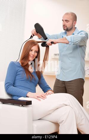 Feb. 01, 2010 - Feb. 1, 2010 - Professional male hairdresser with hair dryer and hair brush drying hair at salon with female red long hair customer Stock Photo