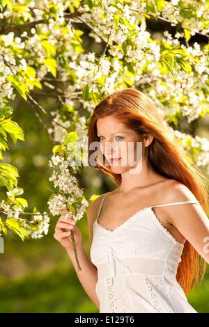 Apr. 25, 2009 - April 25, 2009 - Red hair woman in white dress standing under blooming tree on a sunny day Stock Photo