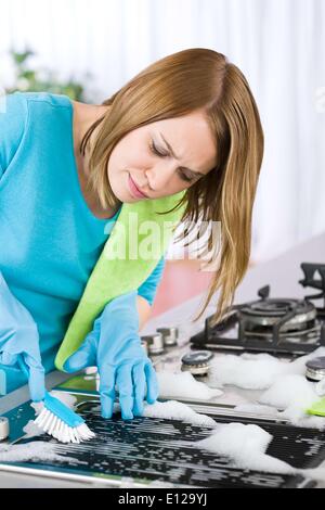 Apr. 01, 2010 - April 1, 2010 - Young woman cleaning stove in modern kitchen with brush and glove Stock Photo