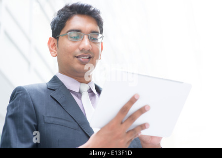 Indian businessman using digital computer tablet, modern office building as background, natural sunlight. Stock Photo