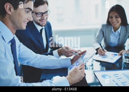 Image of businessman pointing at document in touchpad while interacting with his partner at meeting Stock Photo