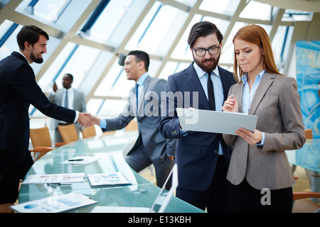 Two business people discussing data or planning work on background of their colleagues handshaking Stock Photo