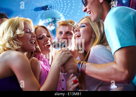 Portrait of joyous guys and girls singing at party in one microphone Stock Photo