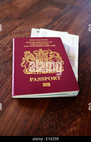 An old EU style pre Brexit burgundy UK Passport with old GBP Sterling bank notes on a dark wood table top. Stock Photo