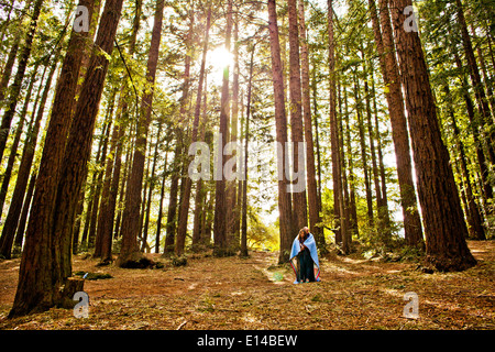 Hispanic couple wrapped in blanket in forest Stock Photo
