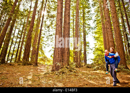 Hispanic man carrying girlfriend piggy back in forest Stock Photo