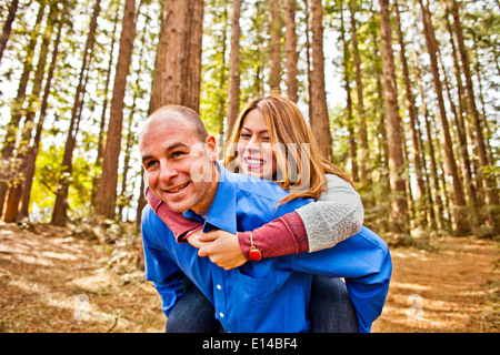 Hispanic man carrying girlfriend piggy back in forest Stock Photo