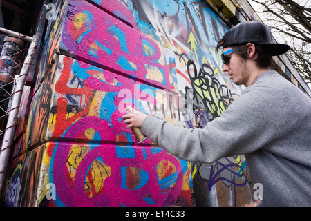 Caucasian boy spraying graffiti on urban wall Stock Photo
