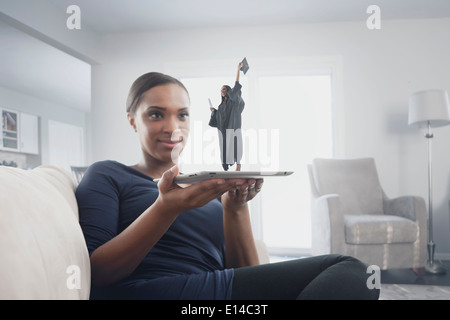 Black woman watching figure of graduate standing on digital tablet Stock Photo