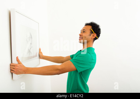 Mixed race man hanging picture on wall Stock Photo