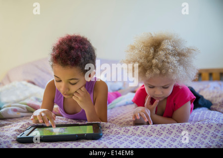 Mixed race sisters using digital tablets in bed Stock Photo