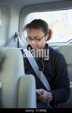 Mixed race girl using digital tablet in back seat of car Stock Photo