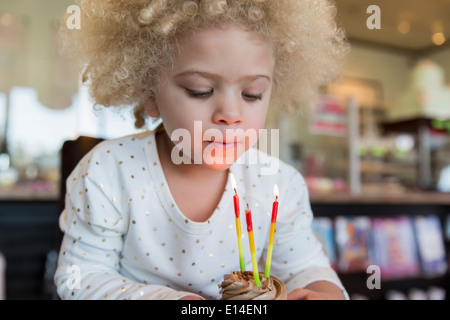 Mixed race girl blowing candles on cupcake Stock Photo