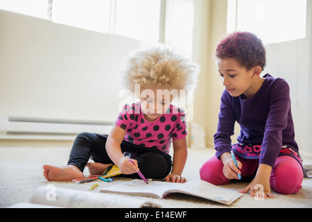 Mixed race sisters coloring on floor Stock Photo