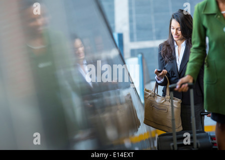 Mixed race businesswoman using cell phone on escalator Stock Photo