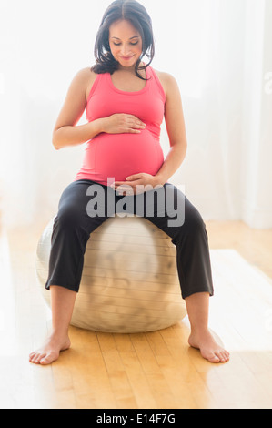 Pregnant Hispanic woman sitting on fitness ball Stock Photo