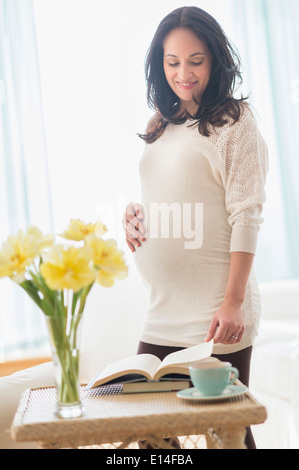 Pregnant Hispanic woman reading book Stock Photo