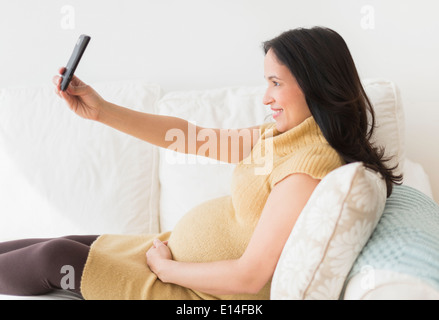 Pregnant Hispanic woman taking picture with cell phone Stock Photo