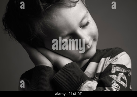 Boy with closed eyes resting his head on his folded hands as if sleeping Stock Photo