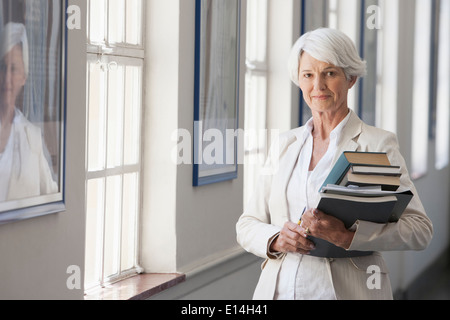 Senior Caucasian businesswoman carrying books in office Stock Photo