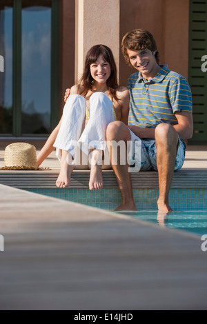 Couple sitting by swimming pool Stock Photo