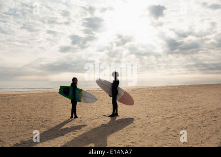 Surfers carrying boards on beach Stock Photo