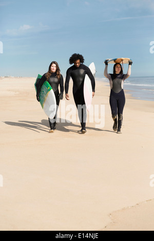 Surfers carrying boards on beach Stock Photo