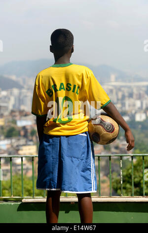 Boy holding a soccer boy and wearing a Brazil jersey while overlooking the centre of Rio de Janeiro, Rio de Janeiro State Stock Photo