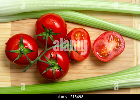 High angle view of bunch of fresh tomatoes and celery sticks on wooden chopping board Stock Photo
