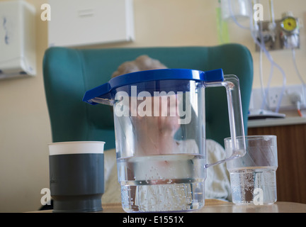Elderly lady in her nineties sitting in chair on hospital ward with jug of water on table. Stock Photo