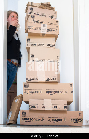 A woman is horrified by a large stack of parcels by Amazon.com in different sizes waiting in front of the entrance door to her f Stock Photo