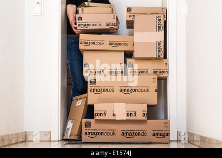A woman is horrified by a large stack of parcels by Amazon.com in different sizes waiting in front of the entrance door to her Stock Photo