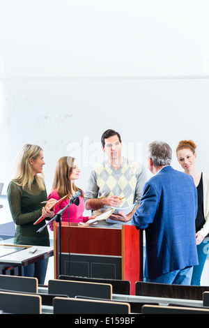 College students making lesson notes while asking professor in university auditorium Stock Photo
