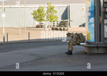 Young male army soldier sits in uniform playing on his smartphone, Glasgow, Scotland, UK Stock Photo