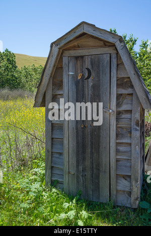 An old wooden outhouse with a half moon cutout in the door in a field outside of the artist community of Harmony, California. Stock Photo