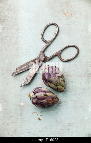 Two whole artichokes and vintage scissors on rustic wooden background Stock Photo