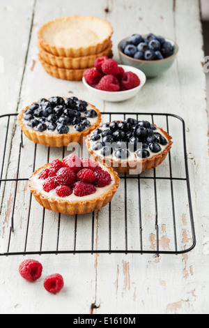 Tartlets with fresh raspberries and blueberries on cooling rack Stock Photo