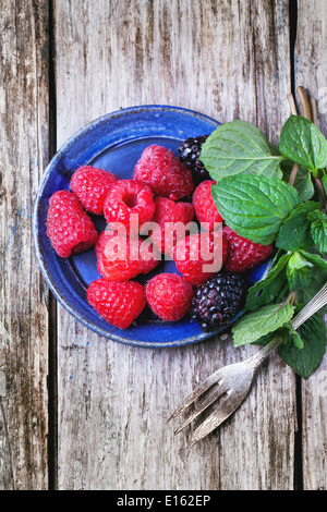 Plate of raspberries and blackberries served with fresh mint and dessert fork over old wooden table. Top view Stock Photo