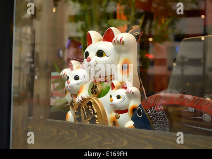 Maneki-neko Japanese lucky cat figurine in a store window featuring a cat and two kittens. Stock Photo