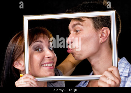 Happy couple in frame. Beautiful young couple looking through a picture frame and smiling  on black Stock Photo