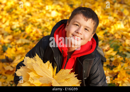 happy smiling caucasian boy with autumn maple leaves on a sunny day in the park Stock Photo