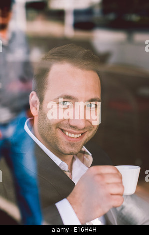 Handsome smiling man drinking espresso in cafe looking through the window Stock Photo
