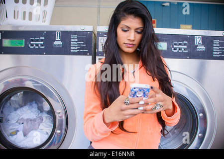 Young woman using smart phone in laundromat Stock Photo
