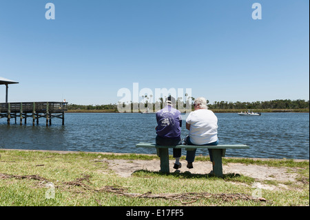 A man and woman sitting on a park bench at Fort Island State Park overlooking Crystal River, Florida watching the boats pass by. Stock Photo