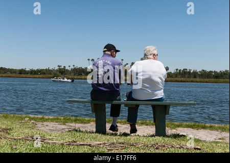 A man and woman sitting on a park bench at Fort Island State Park overlooking Crystal River, Florida watching the boats pass by. Stock Photo