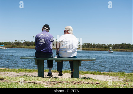 A man and woman sitting on a park bench at Fort Island State Park overlooking Crystal River, Florida watching the boats pass by. Stock Photo