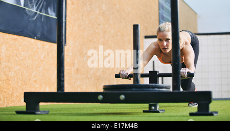 Muscular and strong young female pushing the prowler exercise equipment on artificial grass turf. Fit woman exercising. Stock Photo