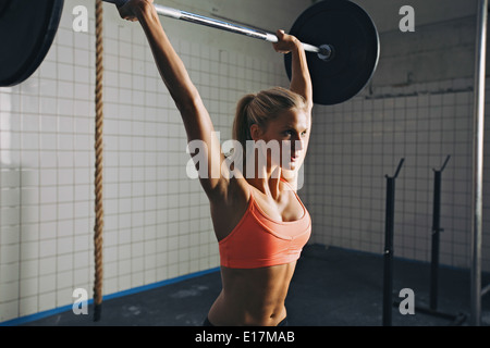 Strong woman lifting barbell as a part of crossfit exercise routine. Fit young woman lifting heavy weights at gym. Stock Photo